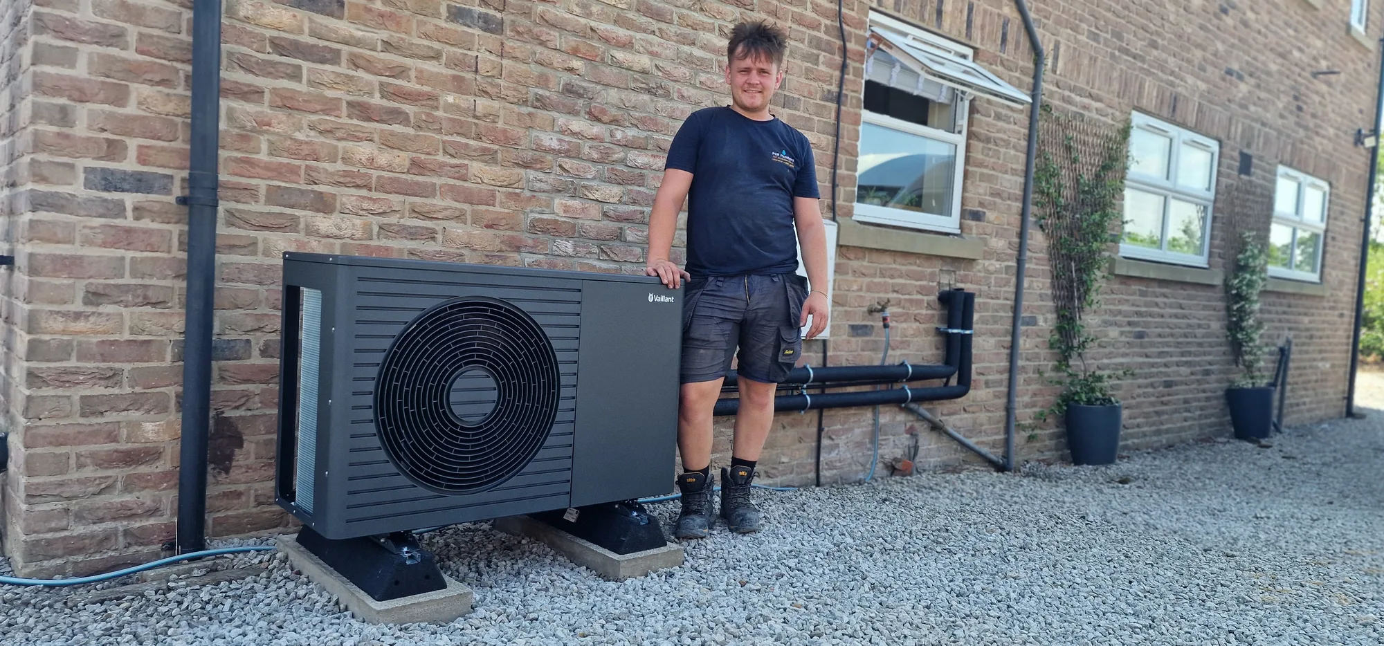 PCR Plumbers heating engineer beside a newly installed Vaillant air-source heat pump at a rural brick property near York and Selby